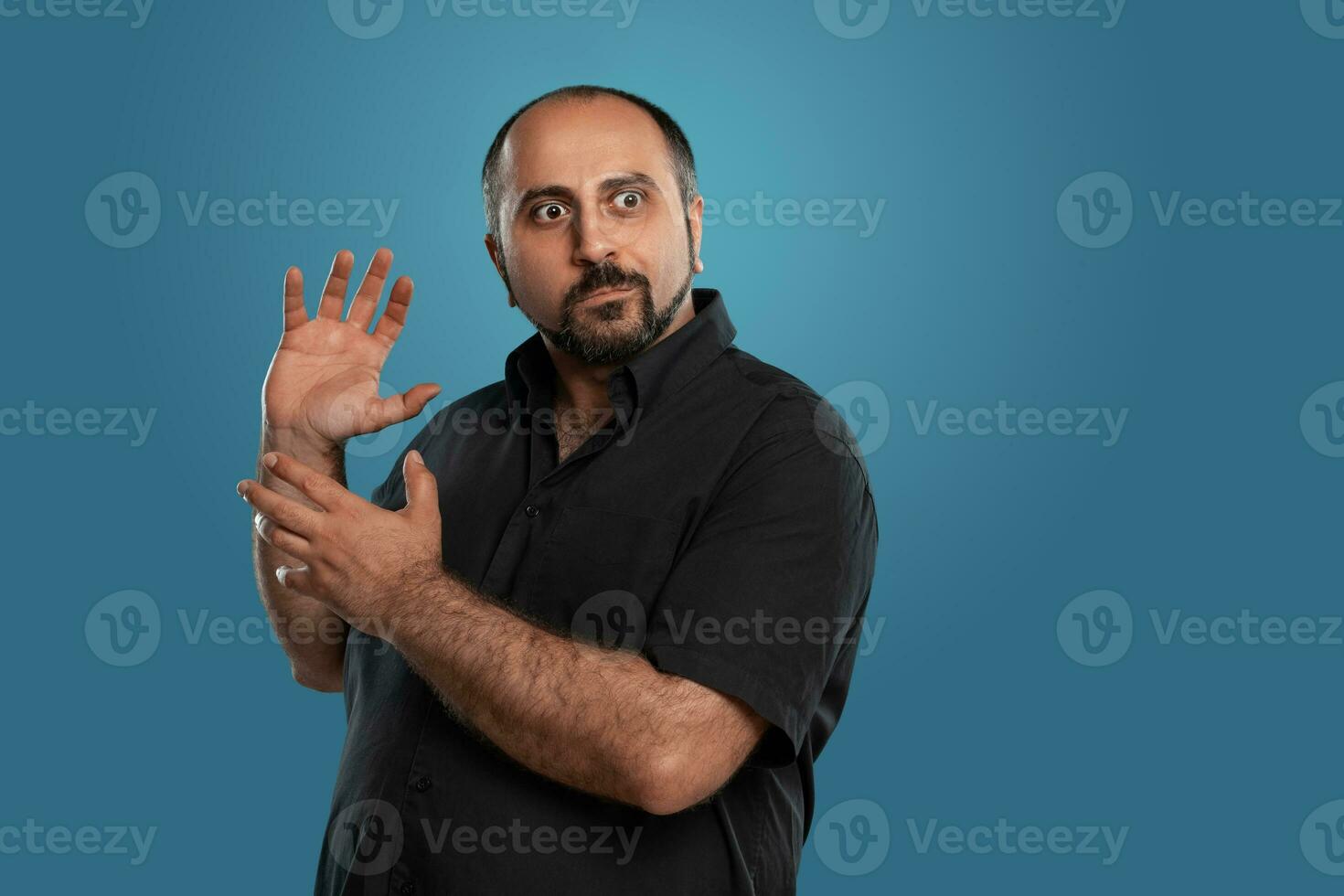 fechar-se retrato do uma moreno meia idade homem com barba, vestido dentro uma Preto camiseta e posando contra uma azul fundo. foto