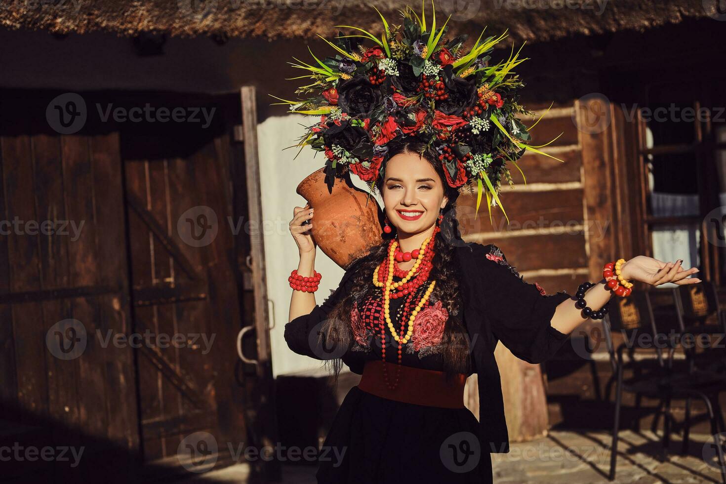 morena menina dentro uma Preto e vermelho ucraniano bordado autêntico nacional traje e uma guirlanda do flores é posando em pé às a portão. foto