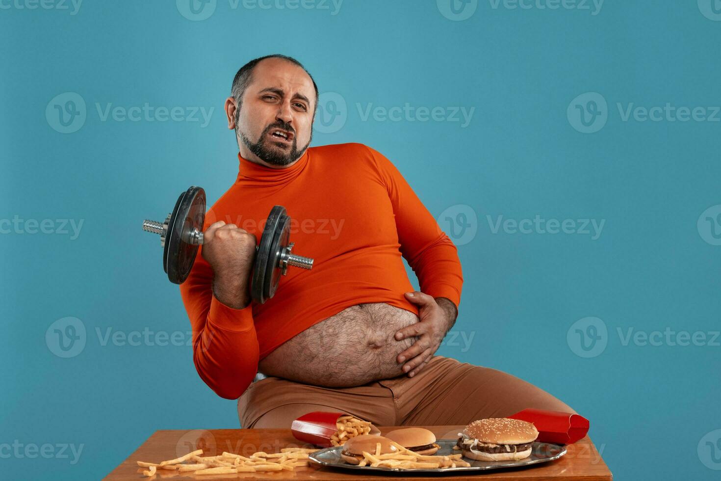 fechar-se retrato do uma meia idade homem com barba, vestido dentro uma vermelho gola alta, posando com hambúrgueres e francês fritas. azul fundo. velozes Comida. foto