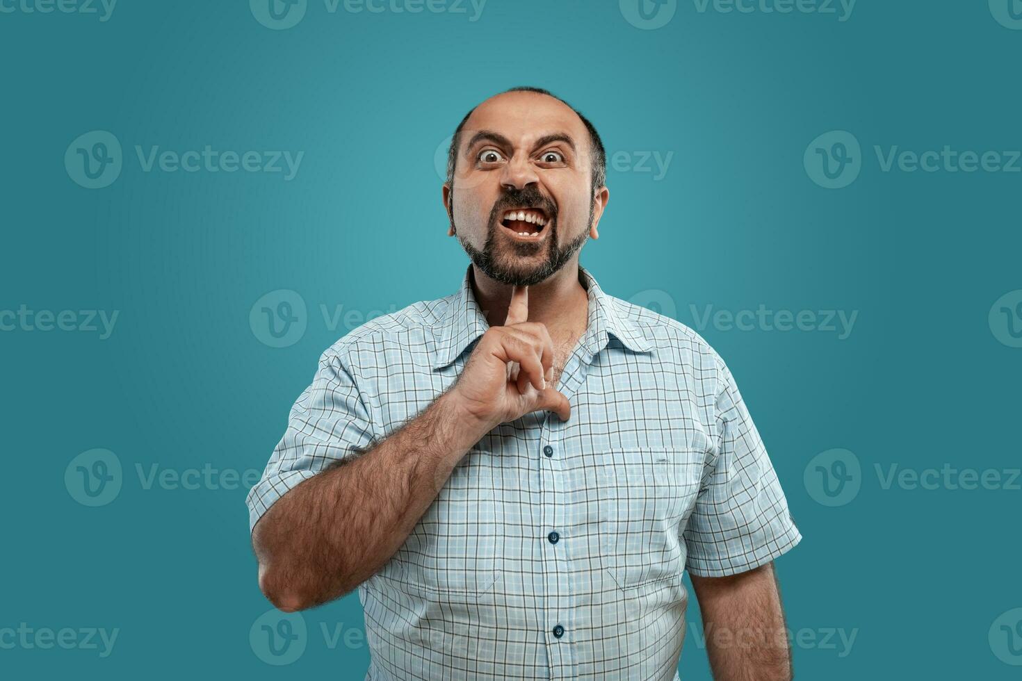 fechar-se retrato do uma moreno meia idade homem com barba, vestido dentro uma luz xadrez camisa e posando contra uma azul fundo. foto