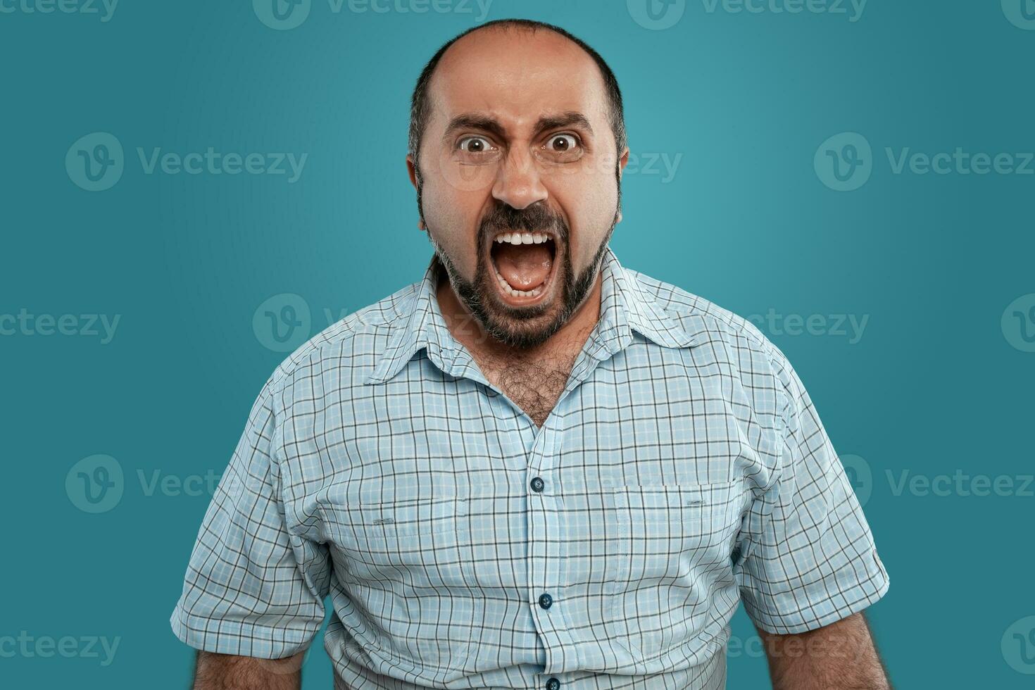 fechar-se retrato do uma moreno meia idade homem com barba, vestido dentro uma luz xadrez camisa e posando contra uma azul fundo. foto