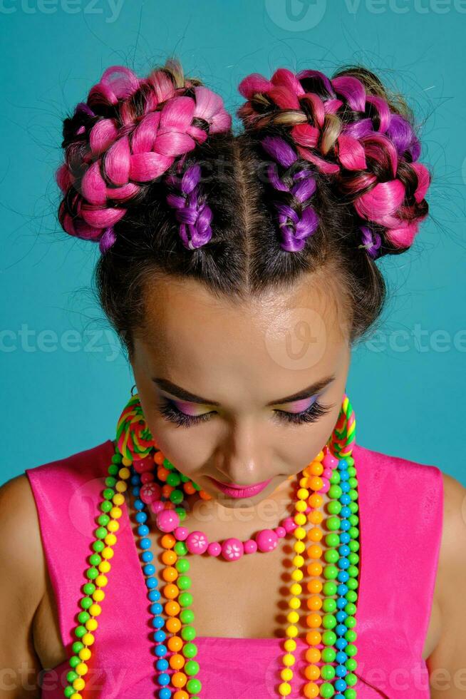 adorável menina com uma multicolorido tranças Penteado e brilhante inventar, posando dentro estúdio contra uma azul fundo. foto