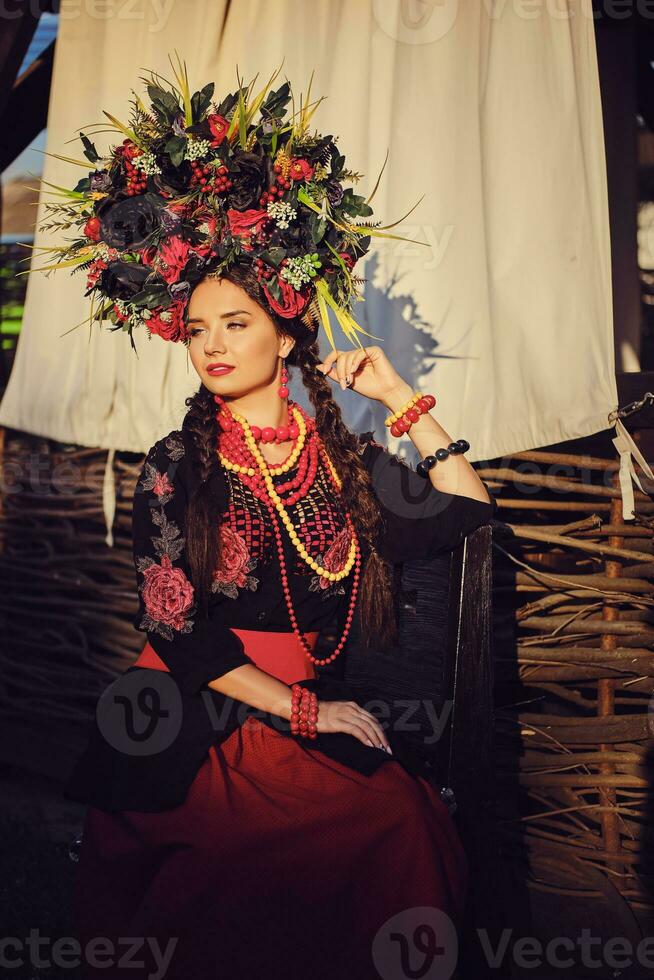 morena menina dentro uma Preto e vermelho bordado ucraniano autêntico nacional traje e uma guirlanda do flores é posando contra uma terraço. fechar-se. foto