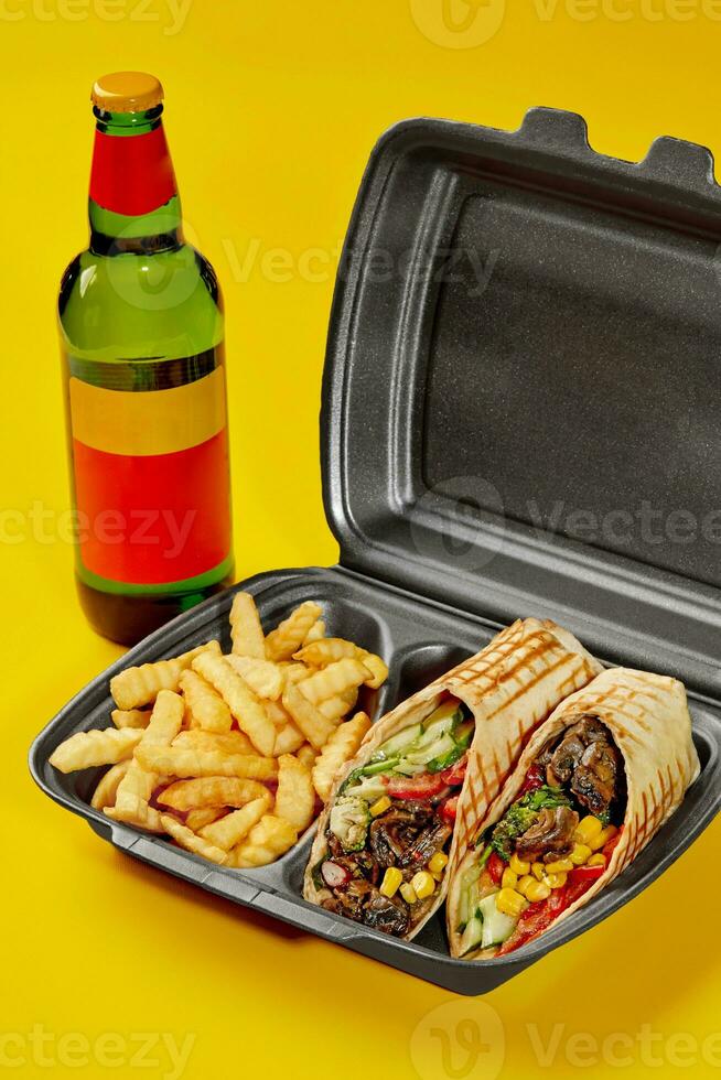 vegano burrito dentro Leve embora recipiente com fritas e garrafa do beber em amarelo fundo foto