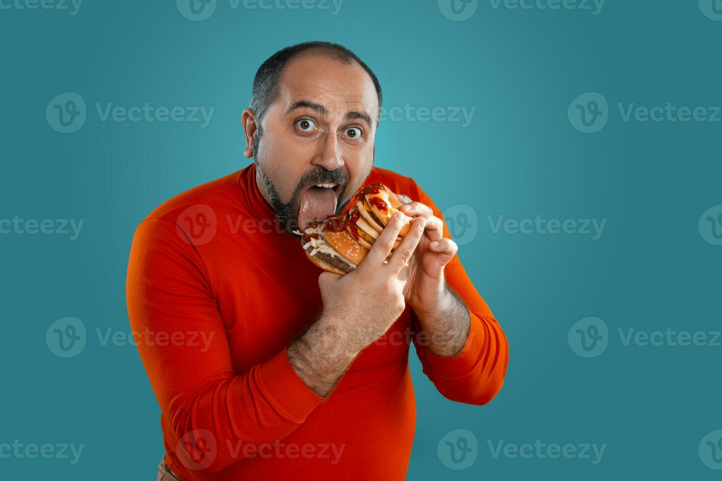 fechar-se retrato do uma meia idade homem com barba, vestido dentro uma vermelho gola alta, posando com hambúrgueres contra uma azul fundo. velozes Comida. foto