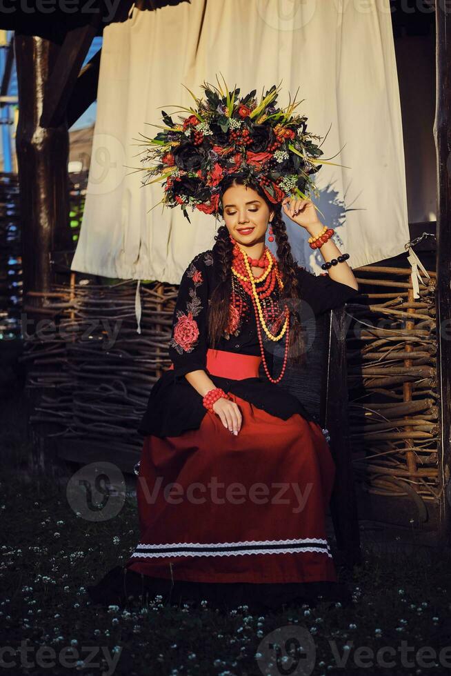 morena menina dentro uma branco ucraniano autêntico nacional traje e uma guirlanda do flores é posando contra uma terraço. fechar-se. foto