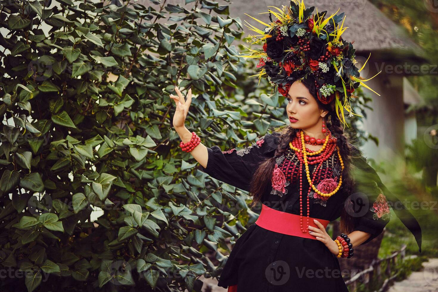 morena menina dentro Preto e vermelho bordado ucraniano autêntico nacional traje e guirlanda do flores é caminhando sozinho e posando dentro uma verde jardim. foto