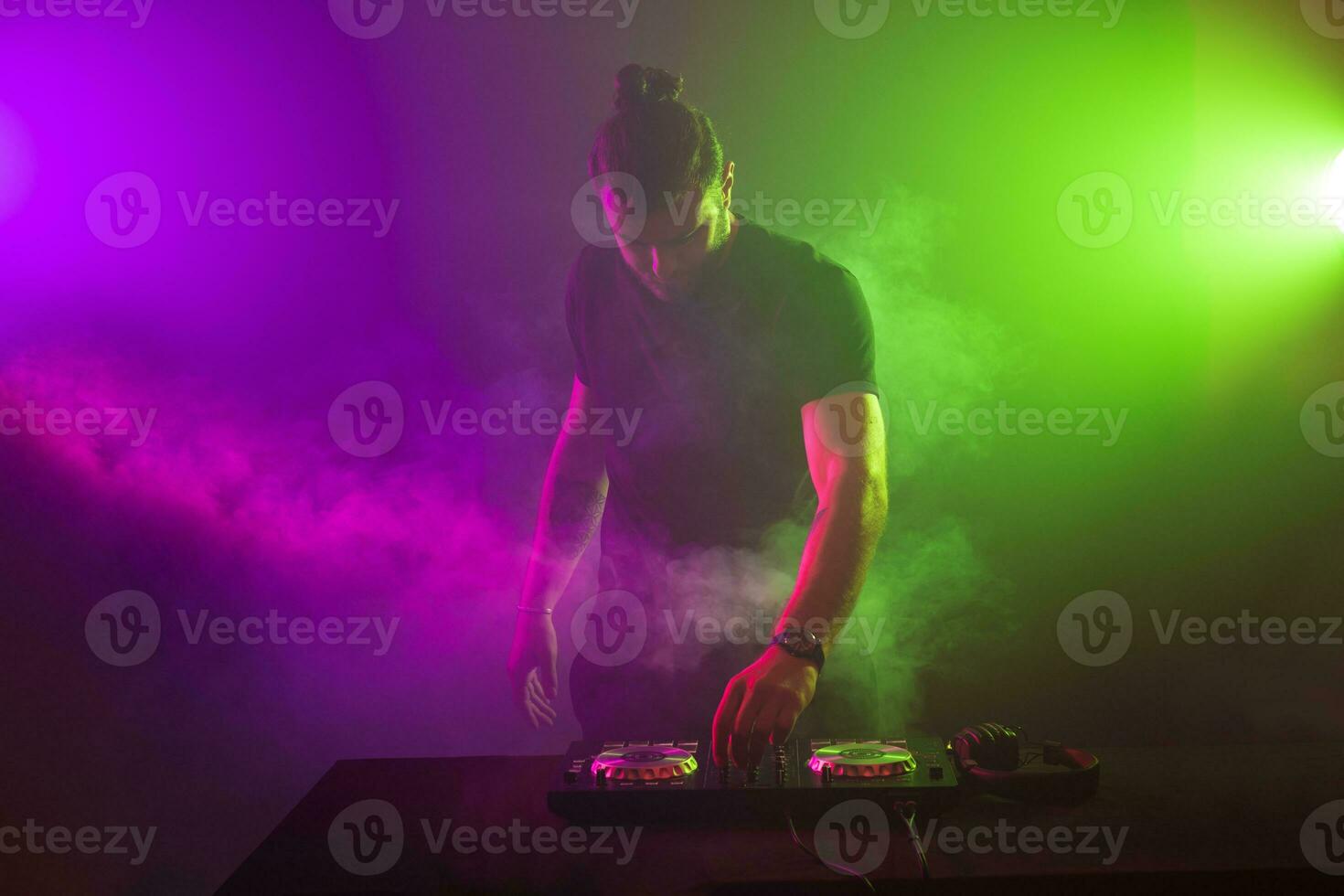 dj às trabalhos mistura som em dela decks às uma festa ou noite clube com colorida fumaça luz fundo foto