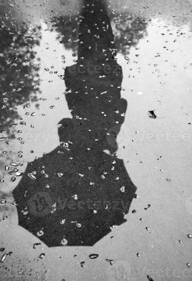 reflexão do uma mulher com a guarda-chuva em molhado calçada durante chuva. Preto e branco. vertical Visão foto