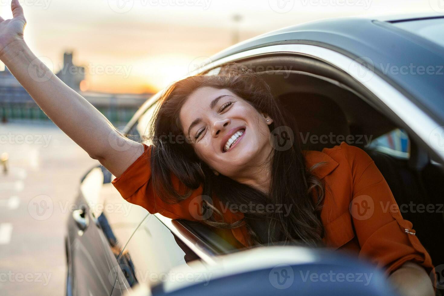 jovem mulher sentada em um carro com a mão para fora da janela. mulher feliz dirigindo um carro e sorrindo. retrato do carro de direção do motorista feminino feliz com cinto de segurança. linda jovem feliz dirigindo o carro. foto