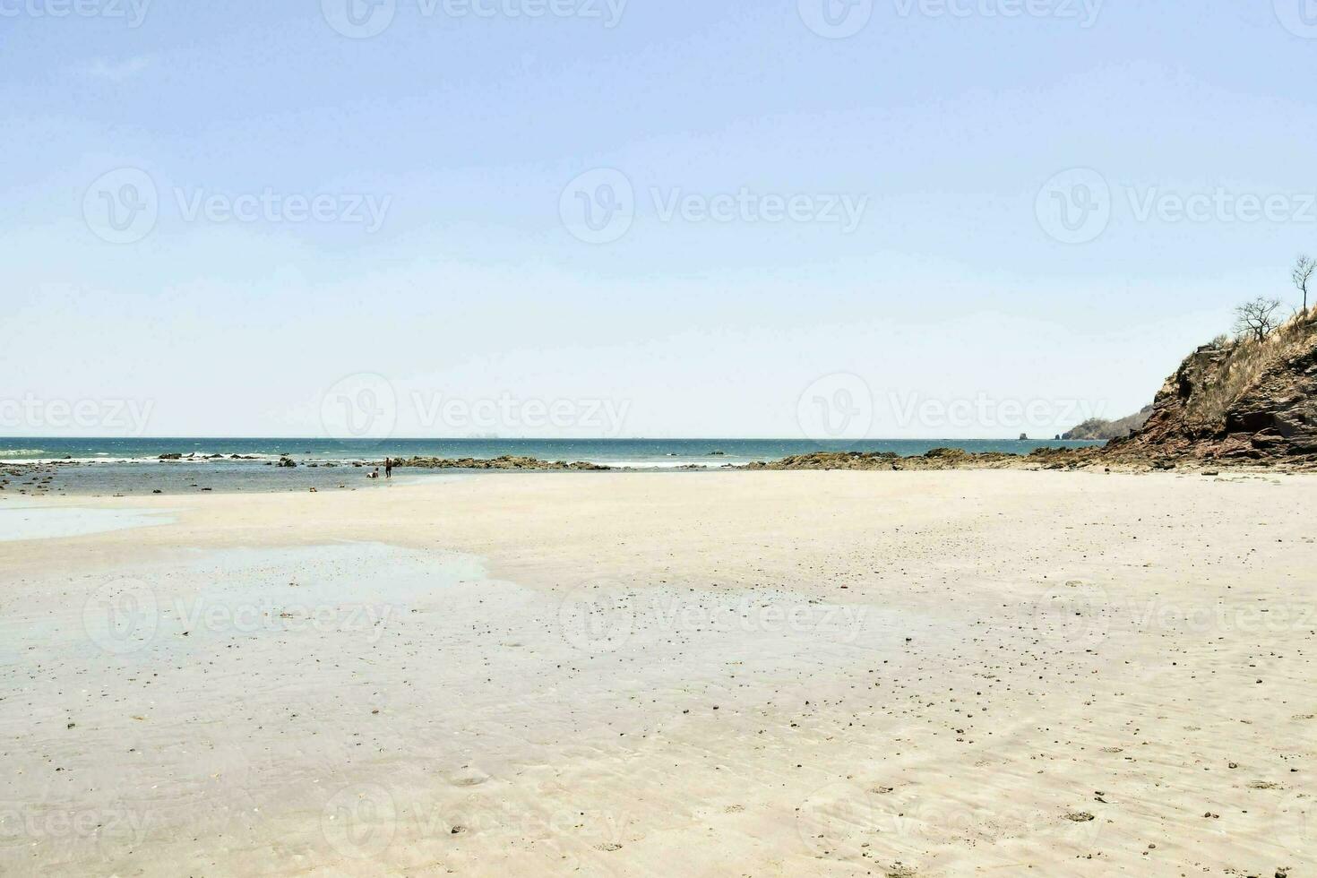 uma arenoso de praia com uma penhasco em a horizonte foto