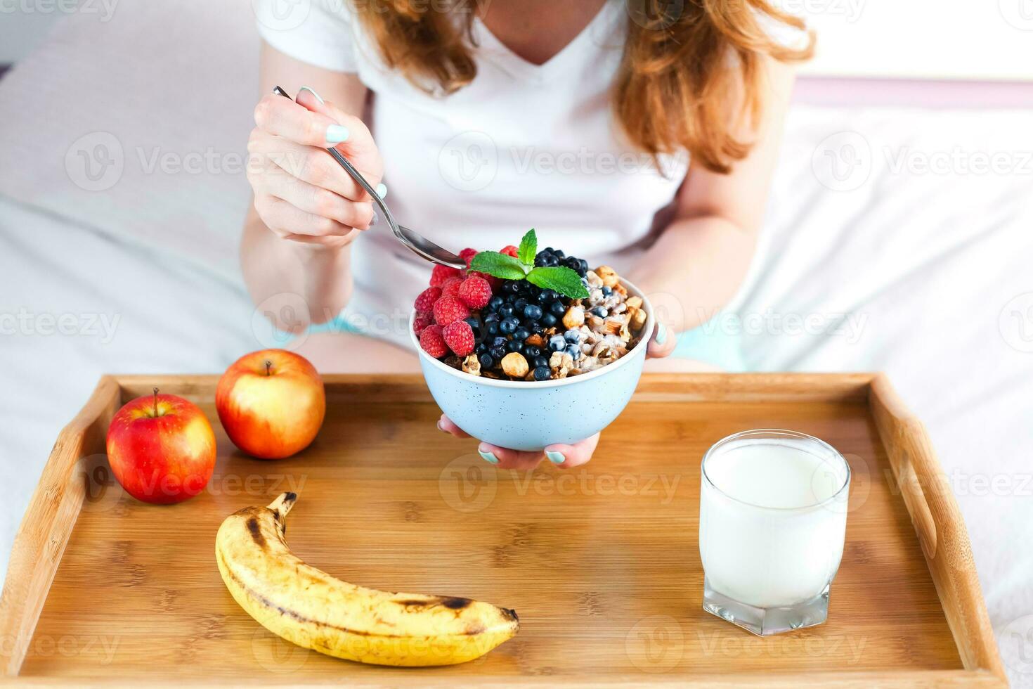 uma jovem menina come granola com fresco bagas para café da manhã em a cama às lar. saudável café da manhã dentro a manhã. foto