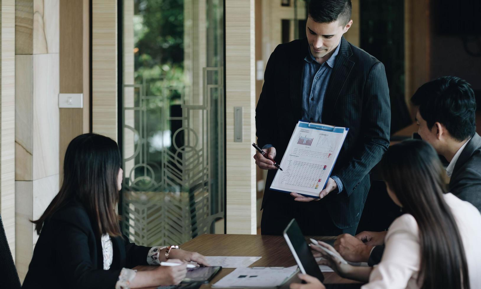 gerente de projeto faz uma apresentação para uma jovem equipe criativa diversificada na sala de reuniões de uma agência. colegas sentam-se atrás da mesa de conferência e discutem o desenvolvimento de negócios foto