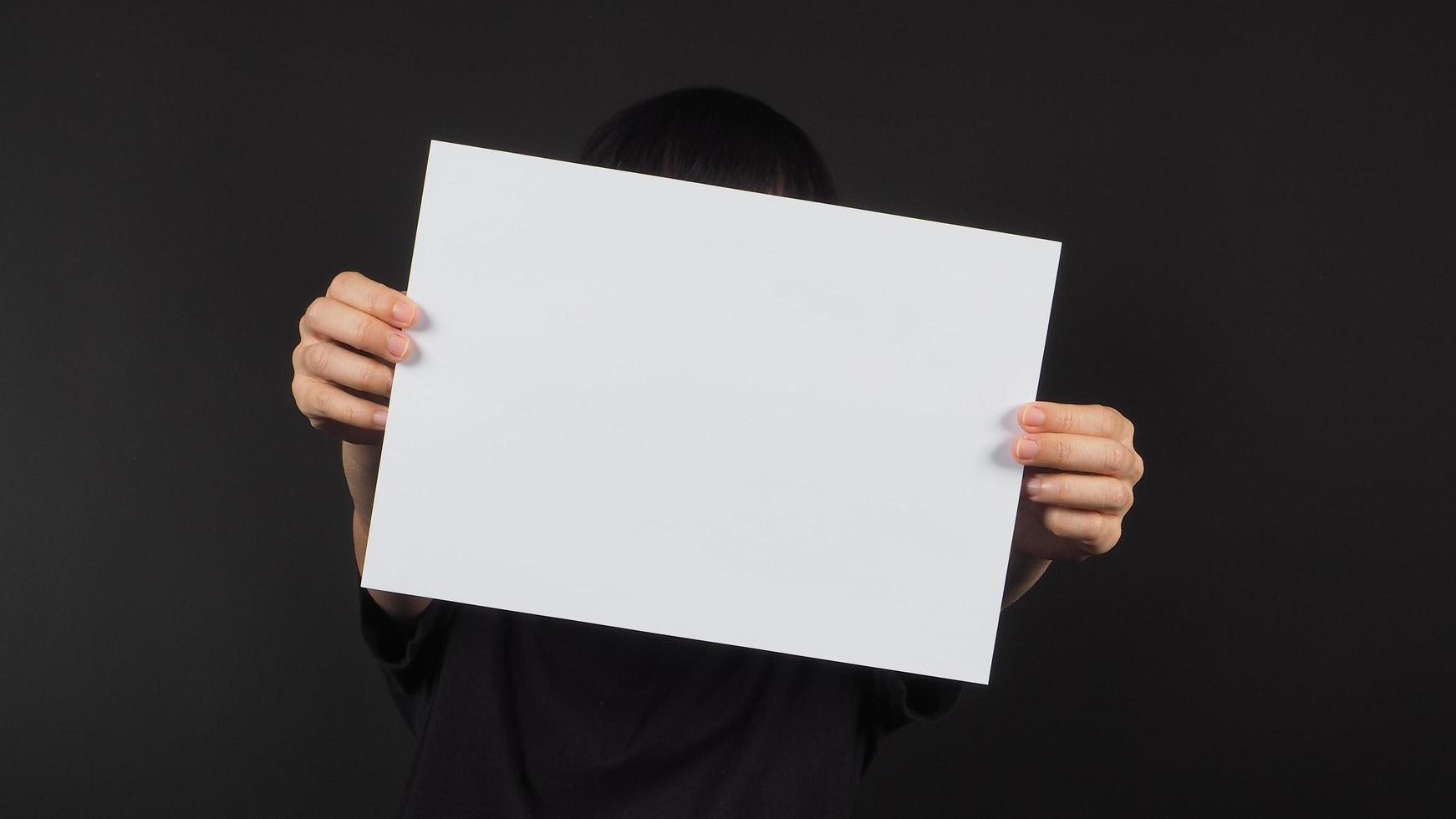 as mãos do modelo feminino estão segurando um papel a4 em branco sobre fundo preto. foto