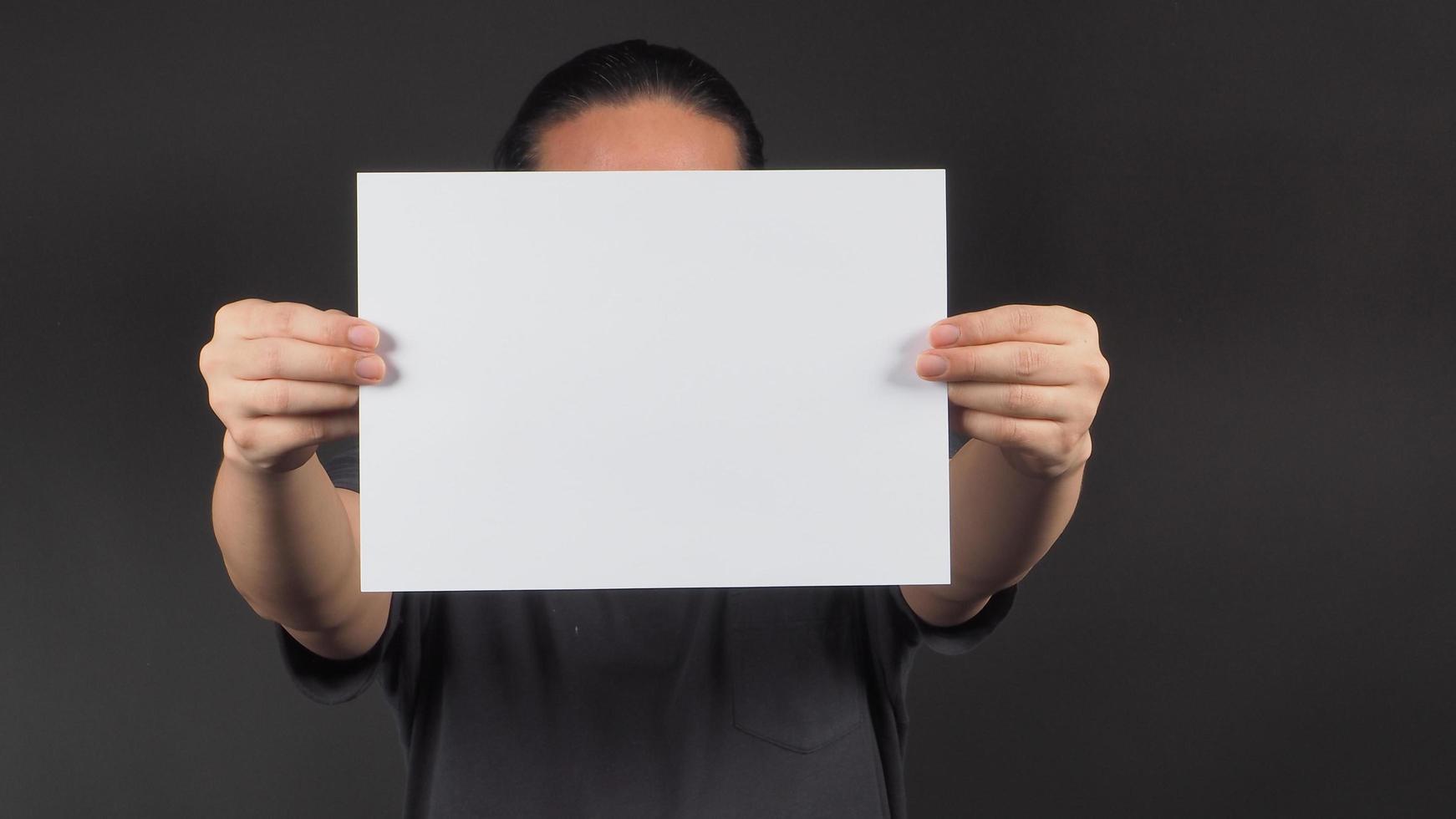 as mãos do modelo masculino estão segurando um papel a4 em branco sobre fundo preto. foto