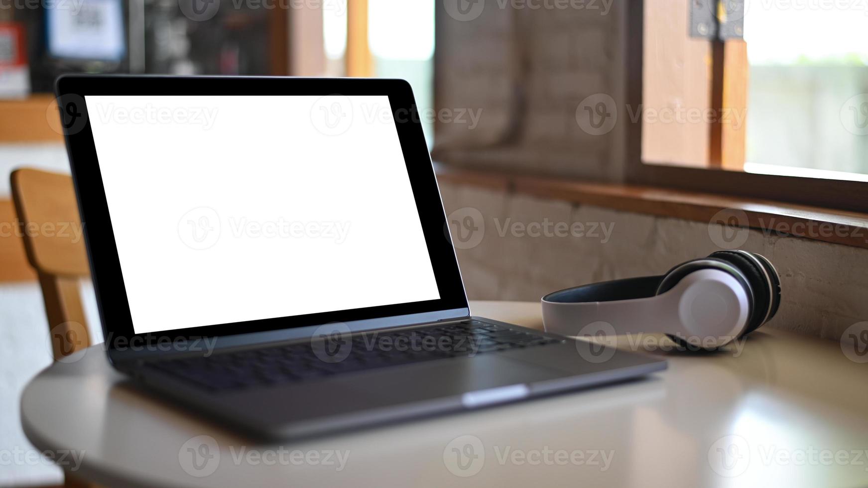 tela em branco do laptop maquete e fone de ouvido colocado sobre uma mesa em um café. foto