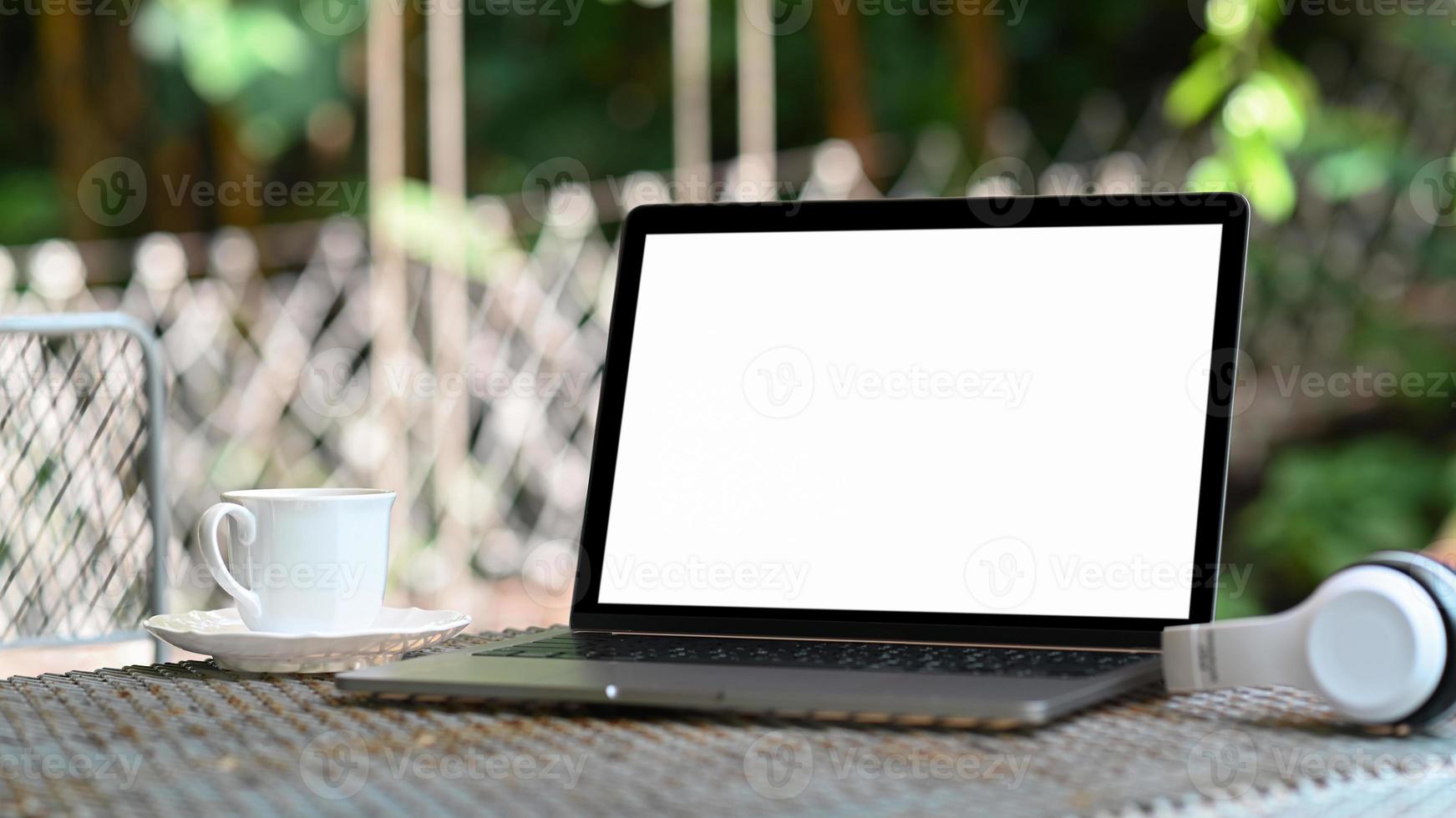 maquete laptop tela branca e caneca de café na mesa com fundo de natureza. foto