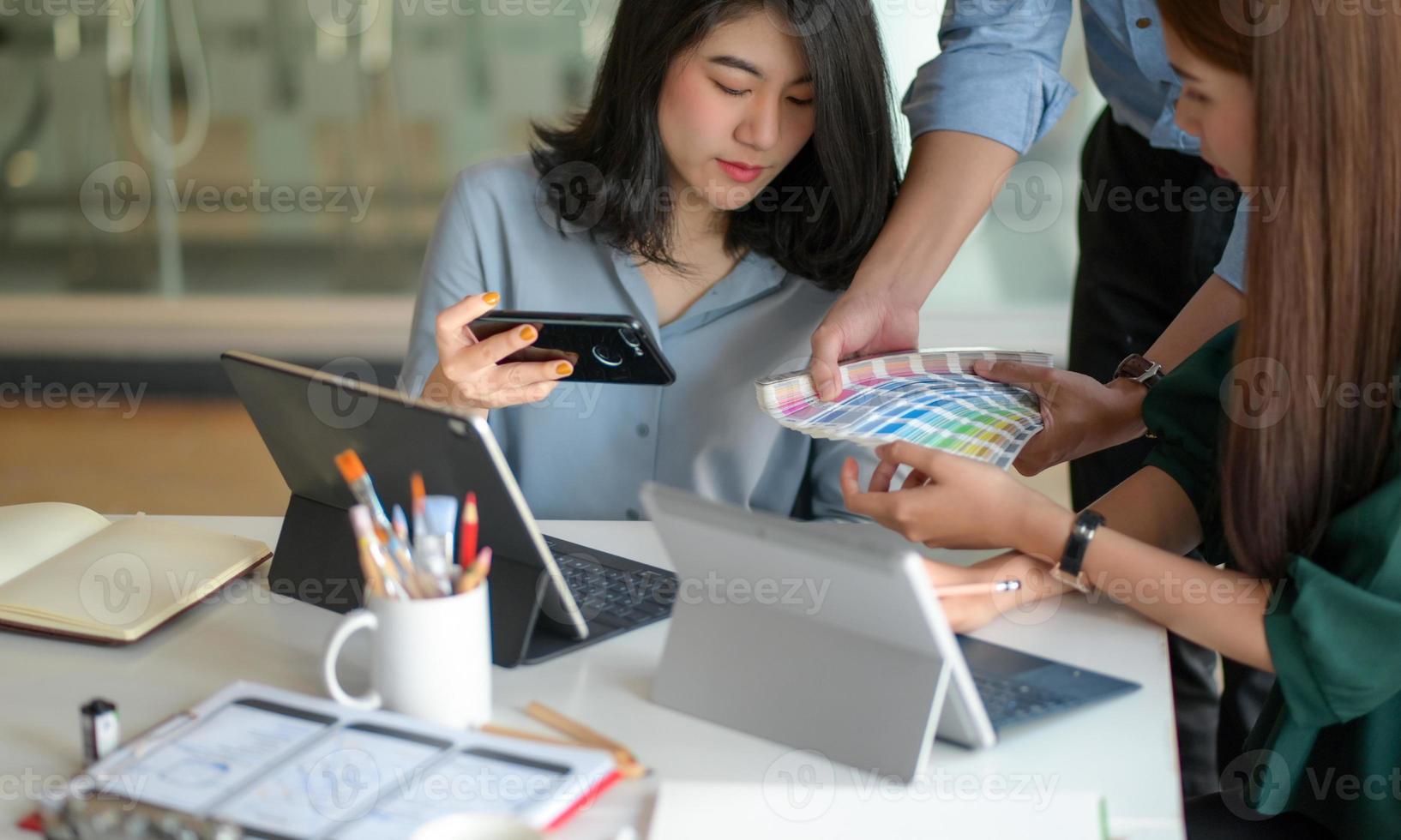 A equipe de designers gráficos está analisando uma tabela de cores para criar um projeto com um laptop e um tablet na mesa. foto