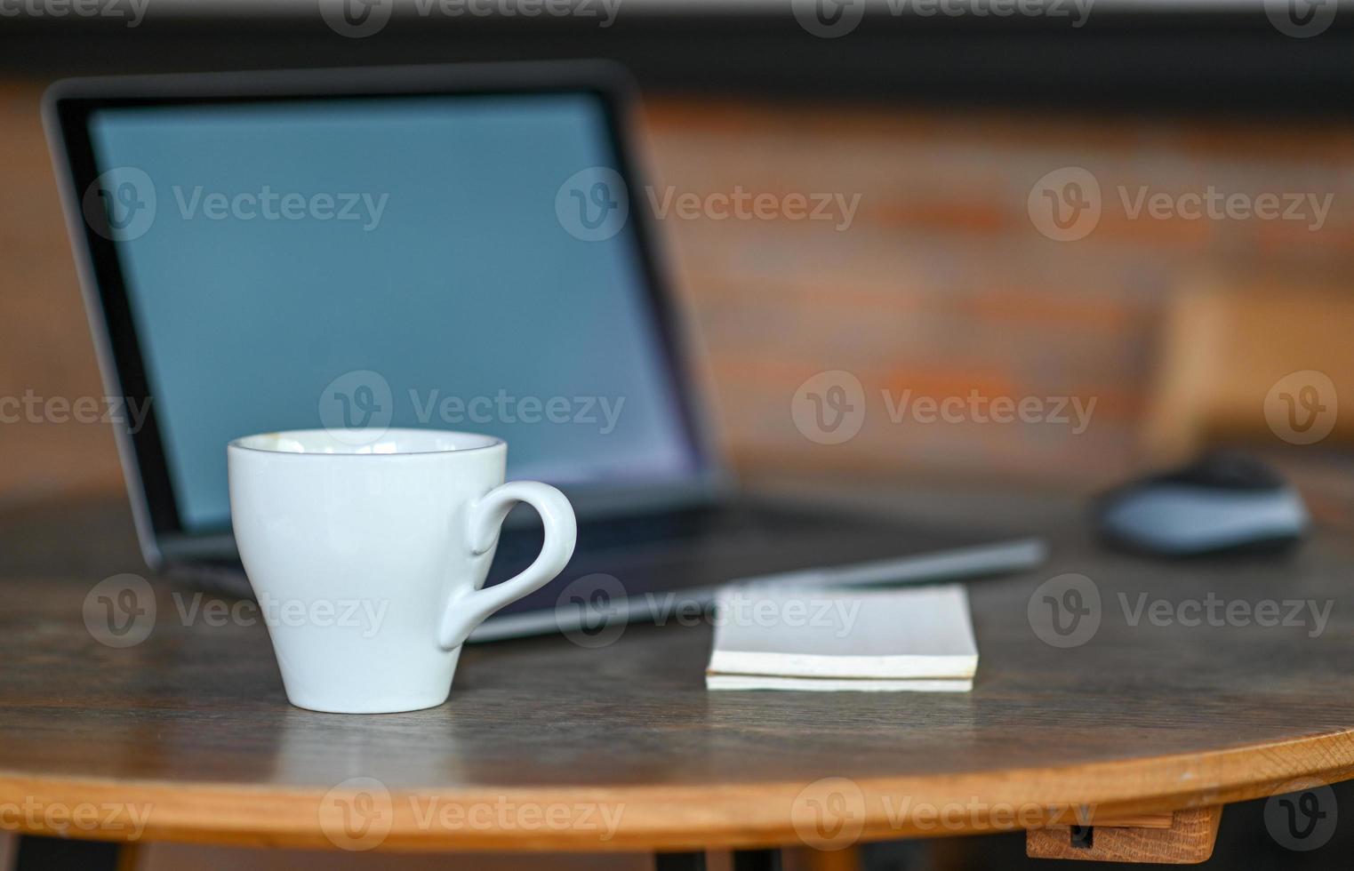 caneca de café branca em cima da mesa com o laptop. foto