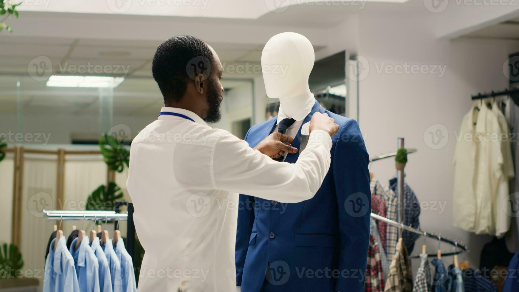 à moda empregado arranjo elegante roupas em manequins dentro luxuoso moda boutique. trabalhador adicionando branco bolso quadrado para Alto rua homens blazer dentro chique roupas loja foto