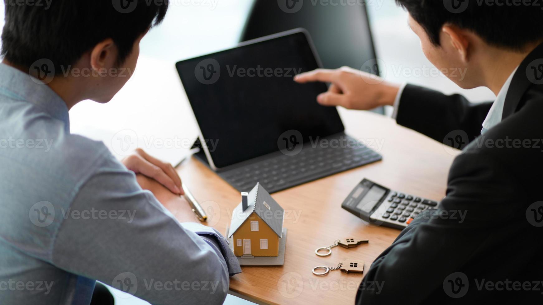 funcionários do banco com laptop recomendando empréstimo hipotecario, modelo da casa e calculadora colocada sobre a mesa. foto