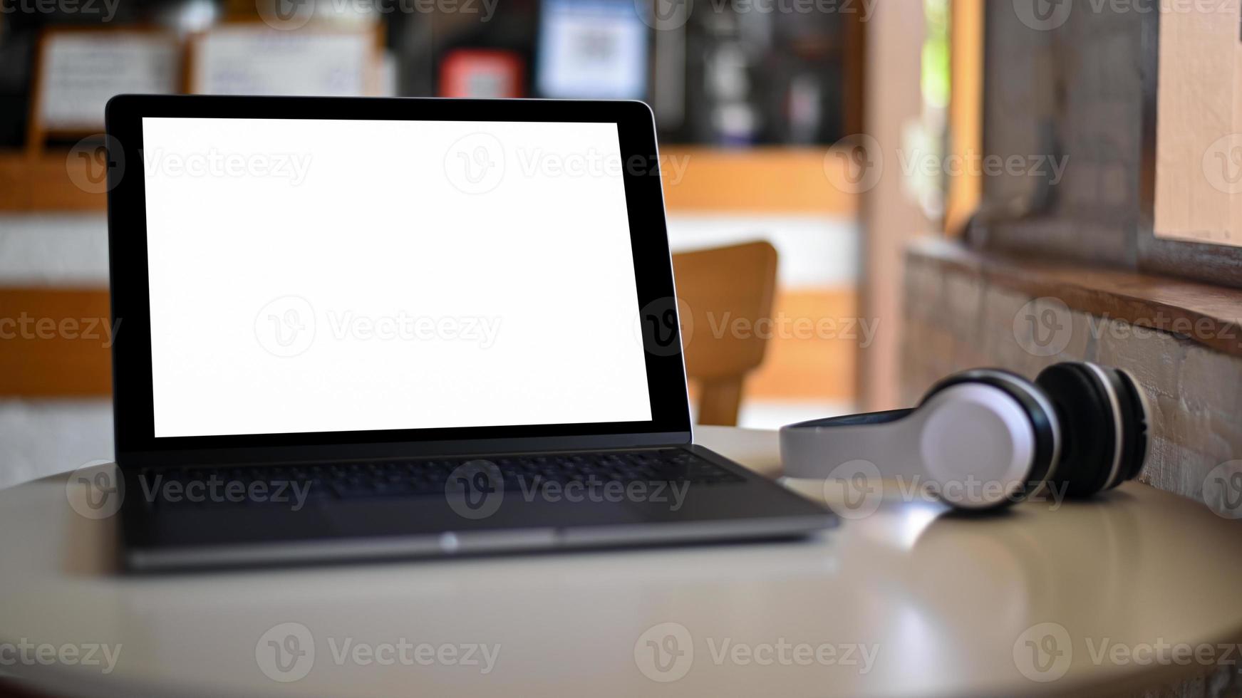 tela em branco do laptop maquete e fone de ouvido colocado sobre uma mesa em um café. foto