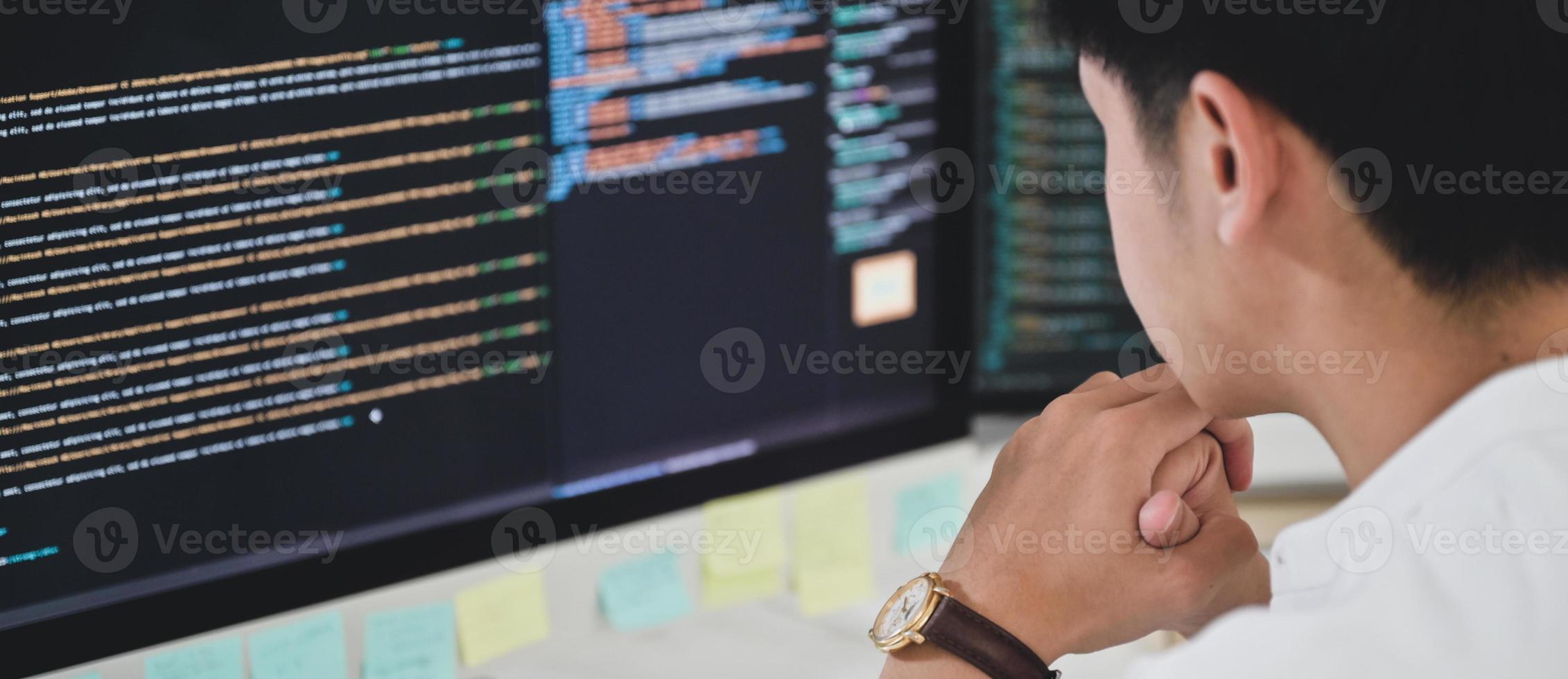 um programador do sexo masculino senta e observa o código em um monitor de computador para verificar a execução do programa. foto