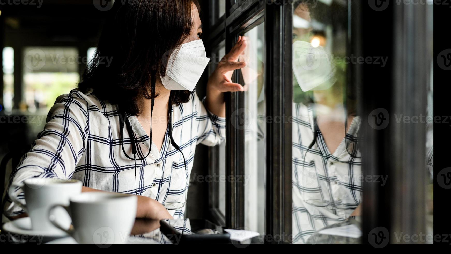 uma mulher usando uma máscara médica sentada em um café, olhando pela janela. foto