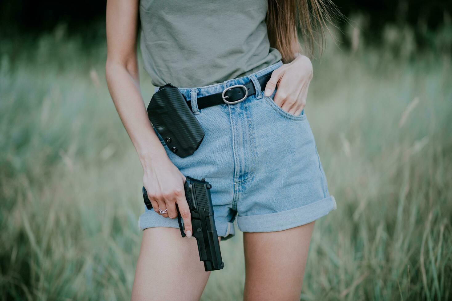 menina dentro jeans calção e com uma arma de fogo dentro dele mão posando dentro a campo. fechar acima foto