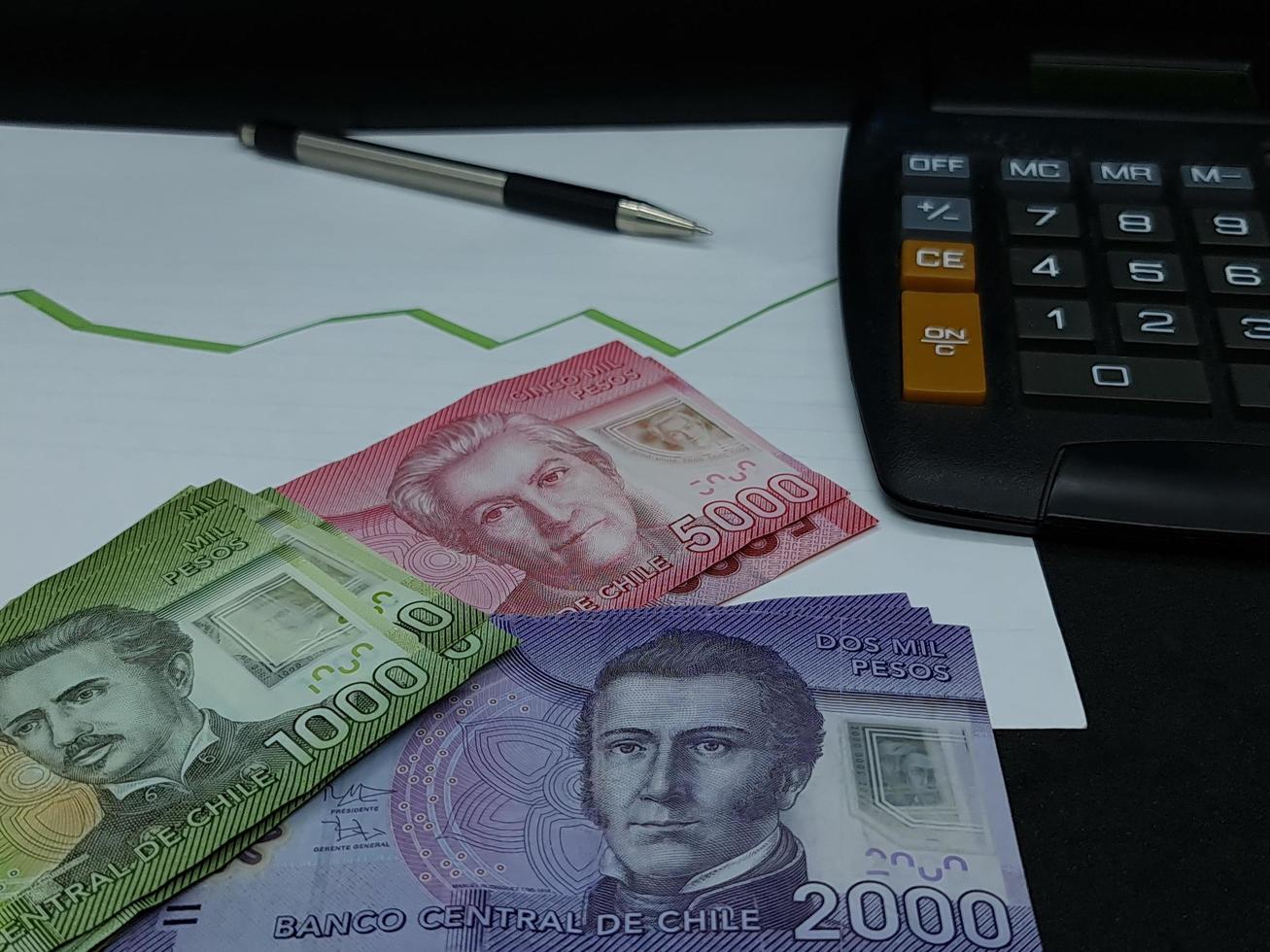 notas, caneta e calculadora chilenas no fundo com linha verde de tendência crescente foto