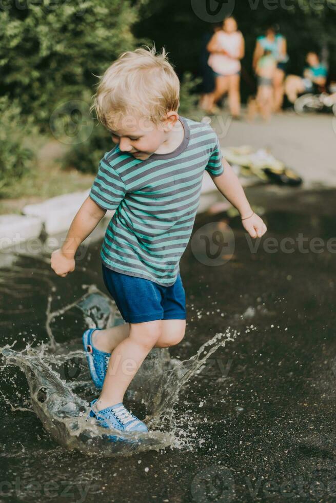 pequeno Garoto pulando dentro uma poça dentro verão foto