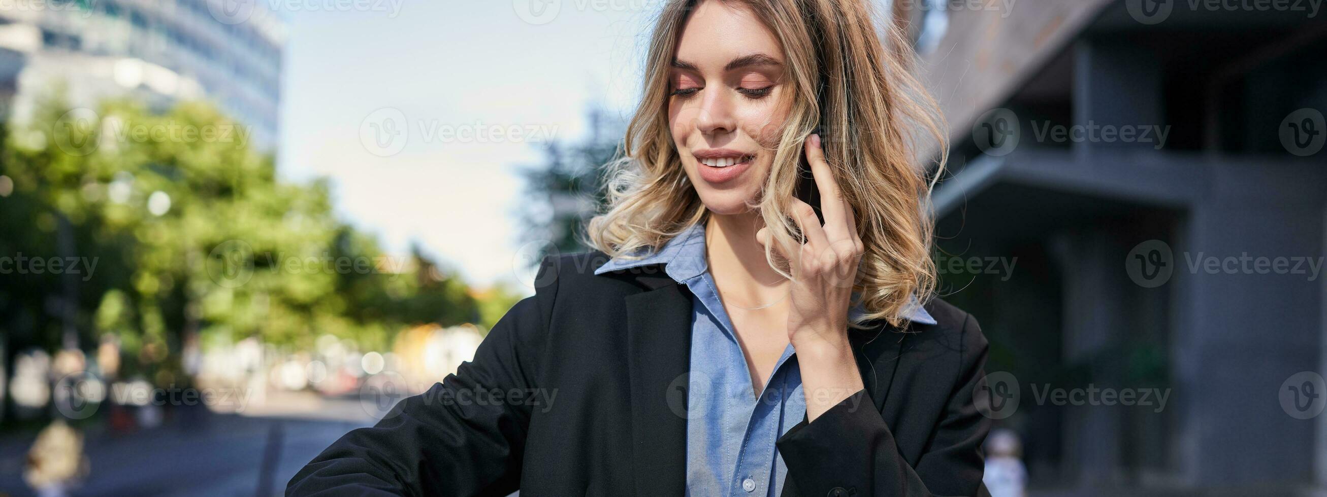 retrato do confiante empresária indo em uma reunião, em pé em rua, falando em Móvel telefone e verificação Tempo em digital Assistir foto