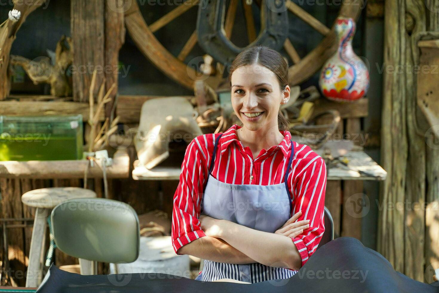 fechar-se bonita artesão fêmea agindo sorrir com braços cruzado dentro dele local de trabalho com Preto couro padronizar para trabalhando. foto