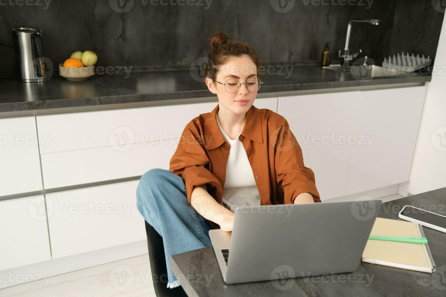 retrato do jovem mulher, aluna dentro cozinha, sentado com computador portátil, trabalhando a partir de lar, estudando ou fazendo trabalho de casa, conecta para conectados bate-papo ou curso a partir de computador foto