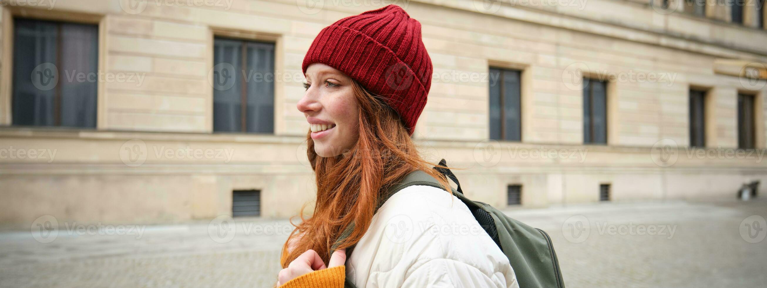 turismo e viajando. jovem ruiva mulher sorridente, turista caminhando com mochila por aí cidade Centro, passeio turístico, detém mochila com papel mapa foto