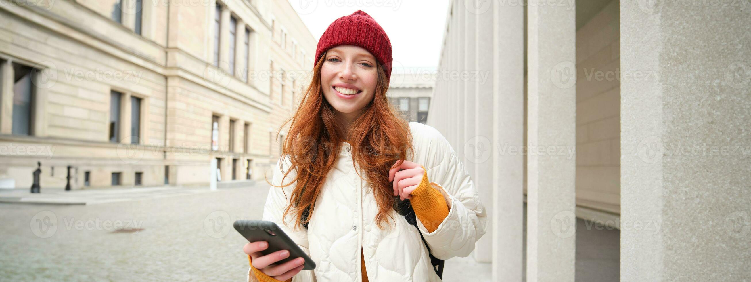 turismo e tecnologia. lindo ruiva menina turista, olhando para uma rota em aplicativo, usando cidade mapa em Smartphone, lendo sobre passeios turísticos lugares em Móvel telefone foto