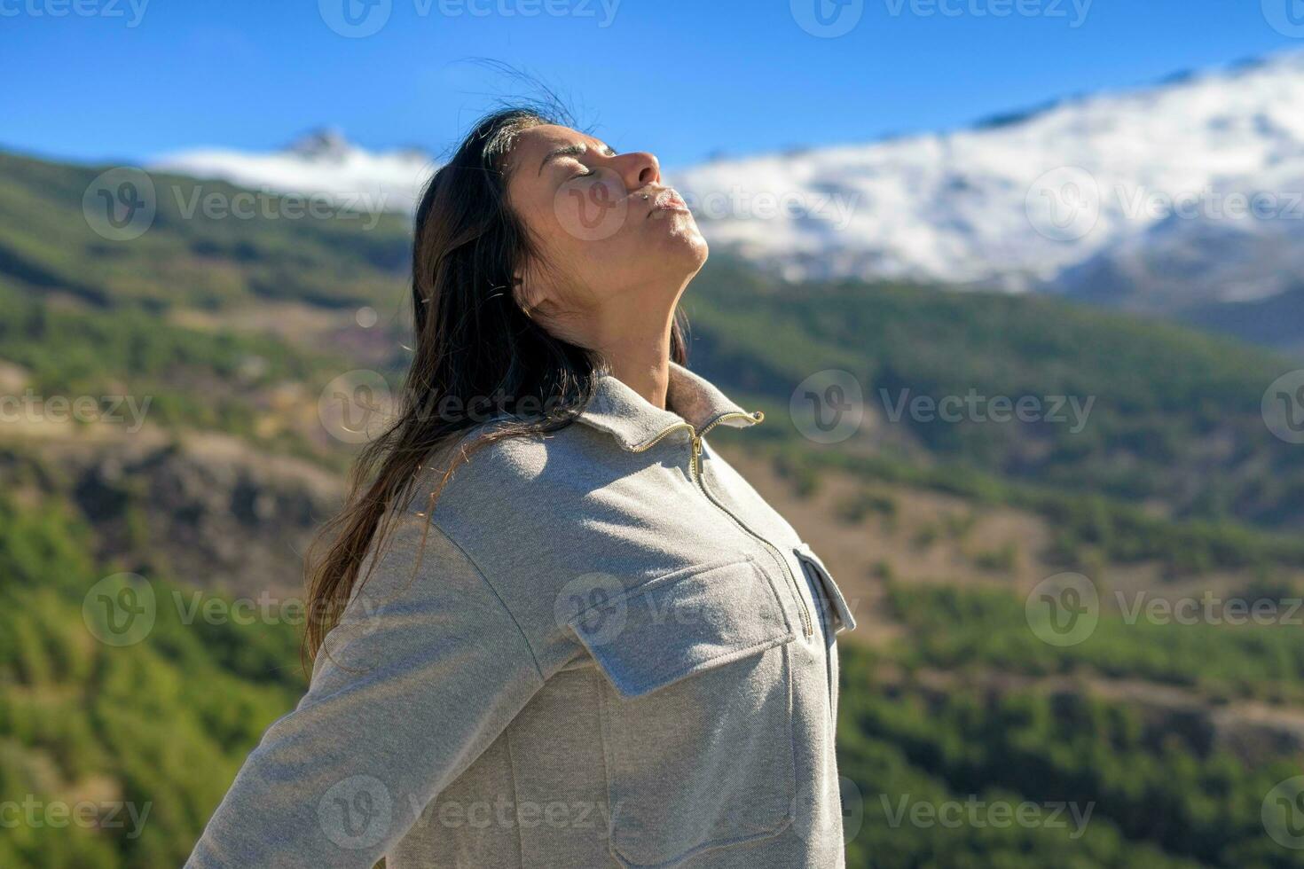 lindo meia idade latina mulher, braços esticado voltar, respiração profundamente, com a Sol dentro frente do dela, Alto dentro a picos do serra Nevada, granada. foto