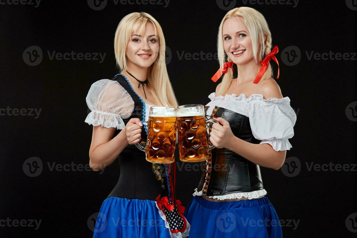 dois lindo Loiras mulheres estão segurando óculos do Cerveja dentro mãos e ficar de pé em Preto fundo dentro estúdio. foto