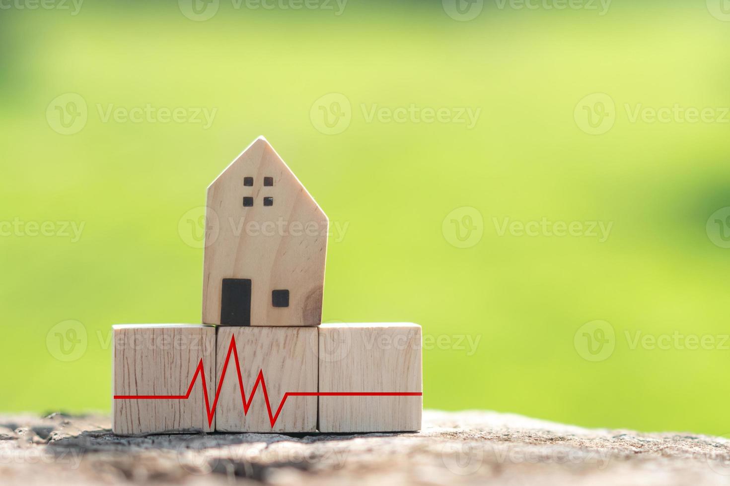 o conceito de dificuldade financeira em tempo de situação de crise é representado por um cubo de madeira com uma maquete de casa e uma pulsação. foto