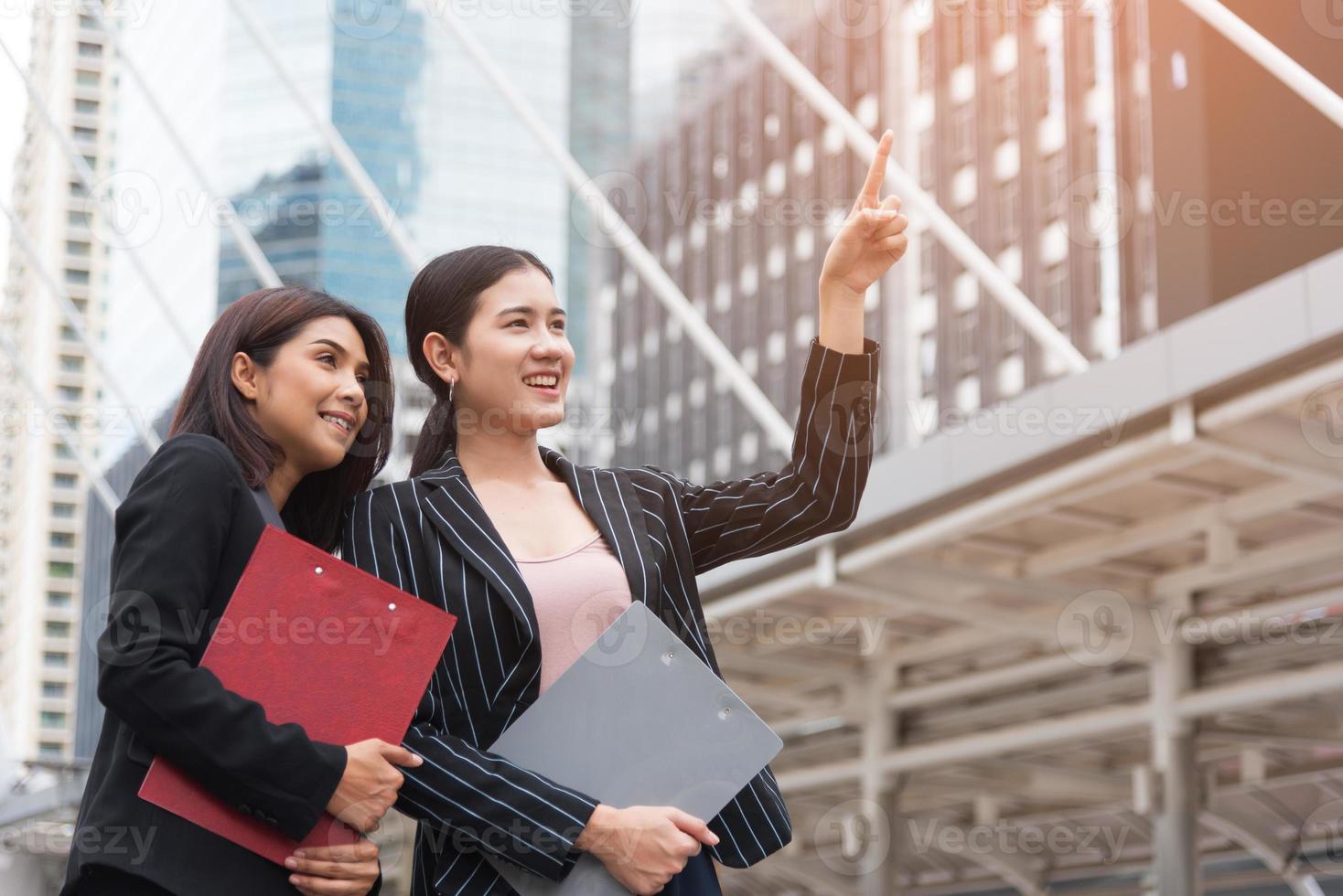 duas mulheres de negócios linda jovem apontando e sorrindo com fundo ao ar livre. conceito de negócios e beleza. conceito de reunião e saudação foto