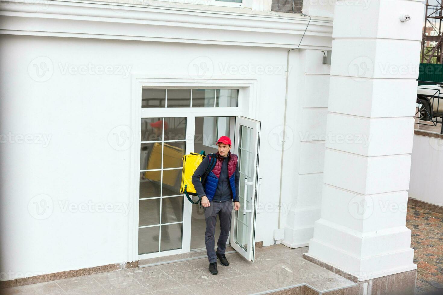 Entrega homem em pé com amarelo termo mochila para Comida Entrega perto a Entrada casa com esvaziar espaço para cópia de colar foto