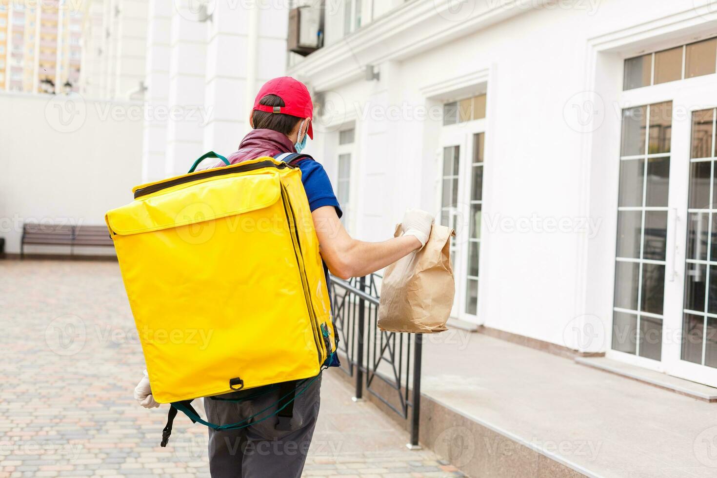 Entrega homem em pé com amarelo termo mochila para Comida Entrega perto a Entrada casa com esvaziar espaço para cópia de colar foto