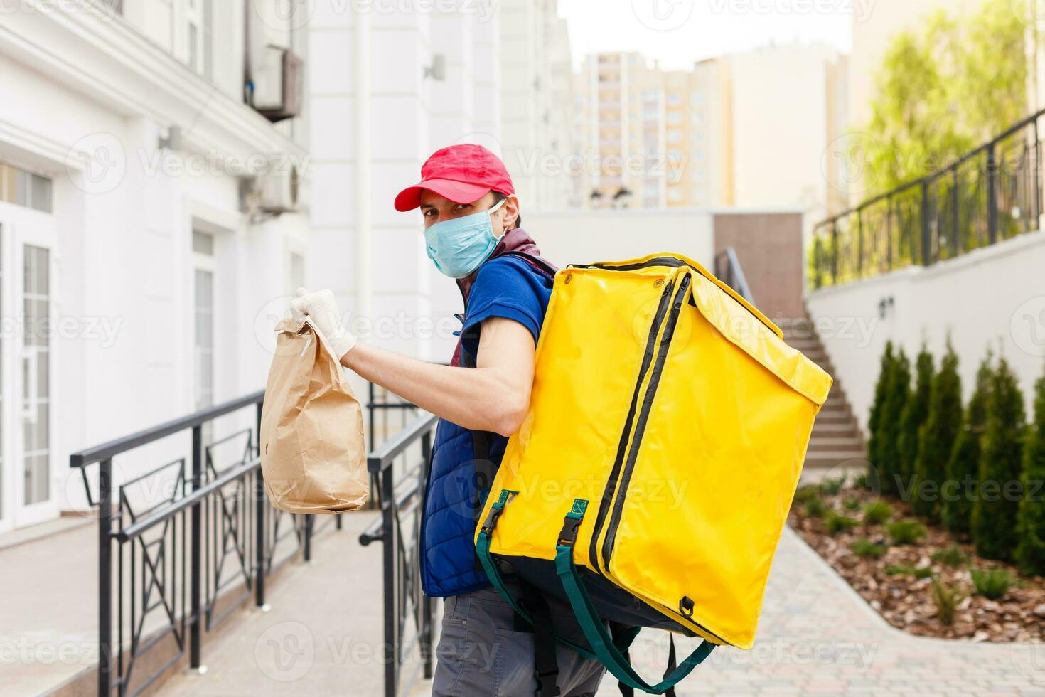 retrato do uma alegre Entrega homem em pé com amarelo termo mochila para Comida Entrega em a rua ao ar livre foto