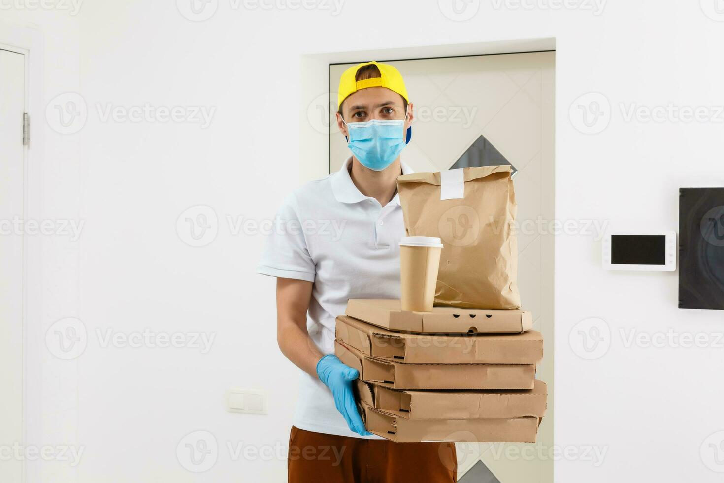 homem a partir de Entrega serviço dentro camiseta, dentro protetora mascarar e luvas dando Comida ordem e segurando pizza caixas sobre branco fundo foto