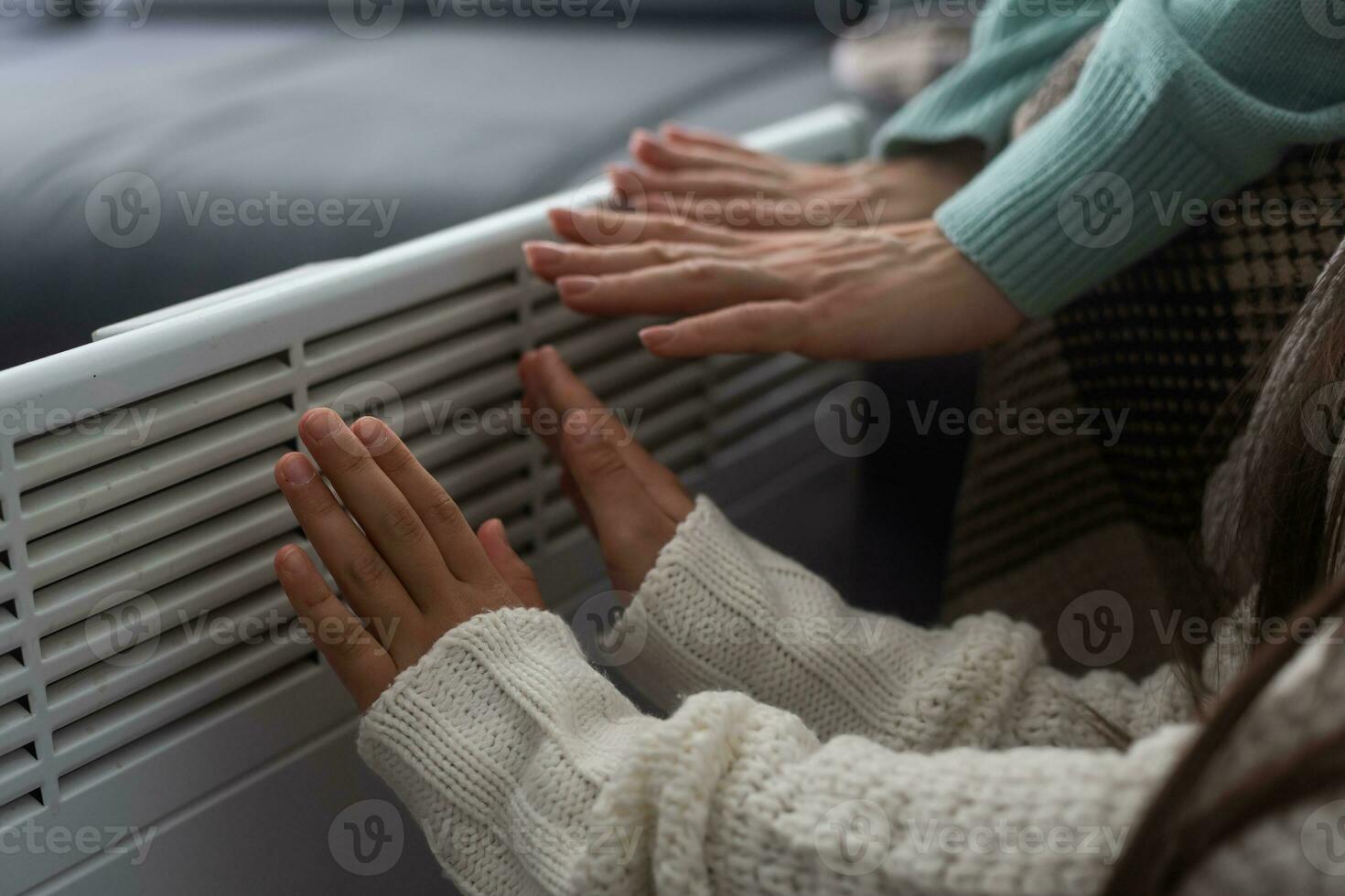 mãe e criança aquecimento mãos perto elétrico aquecedor às lar, fechar-se. foto