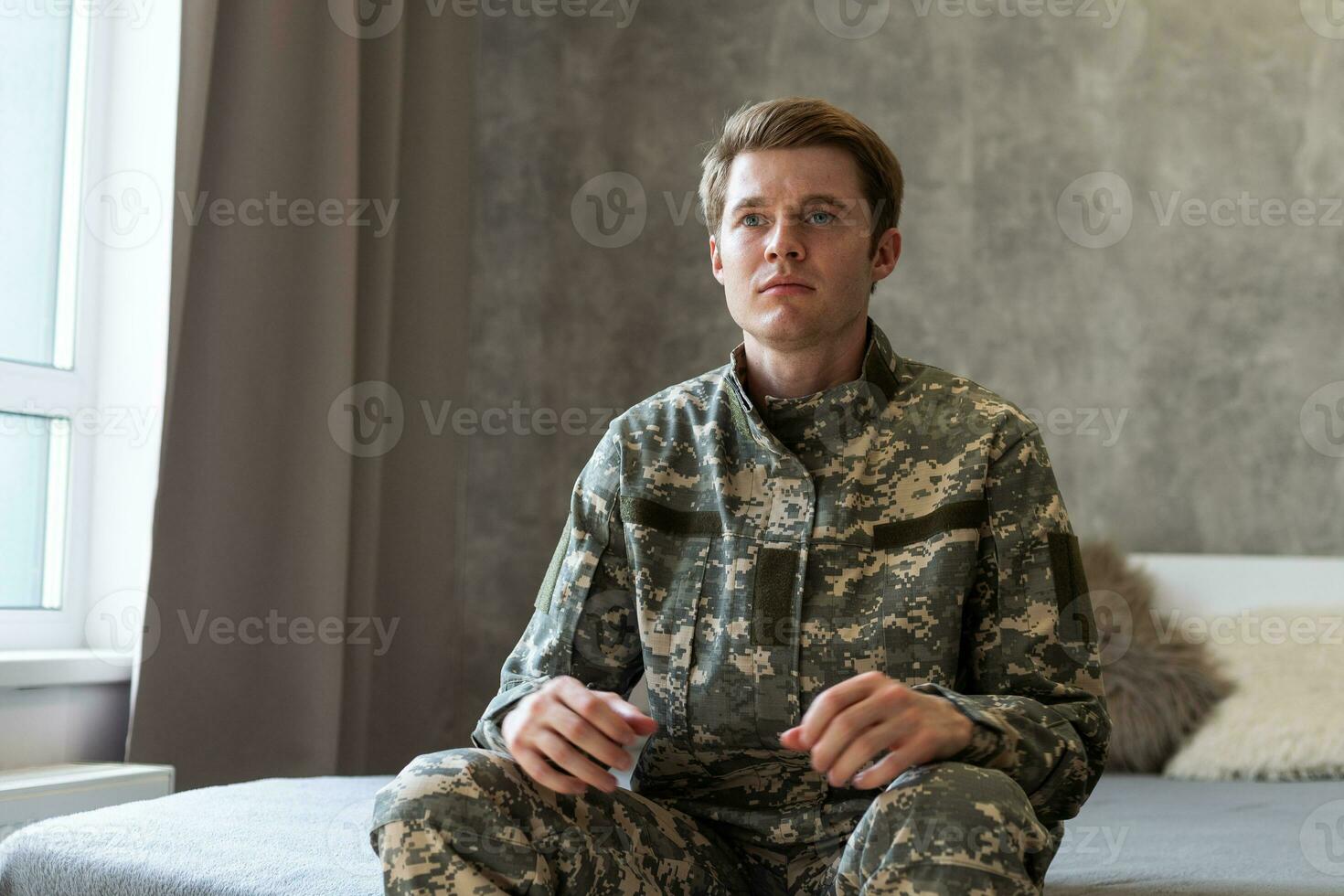 estressado veterano soldado absorta dentro depressivo pensamentos e recordações. triste depressivo jovem militares homem dentro camuflar uniforme sentado em sofá e pensando sobre guerra. ptsd e terapia conceito. foto