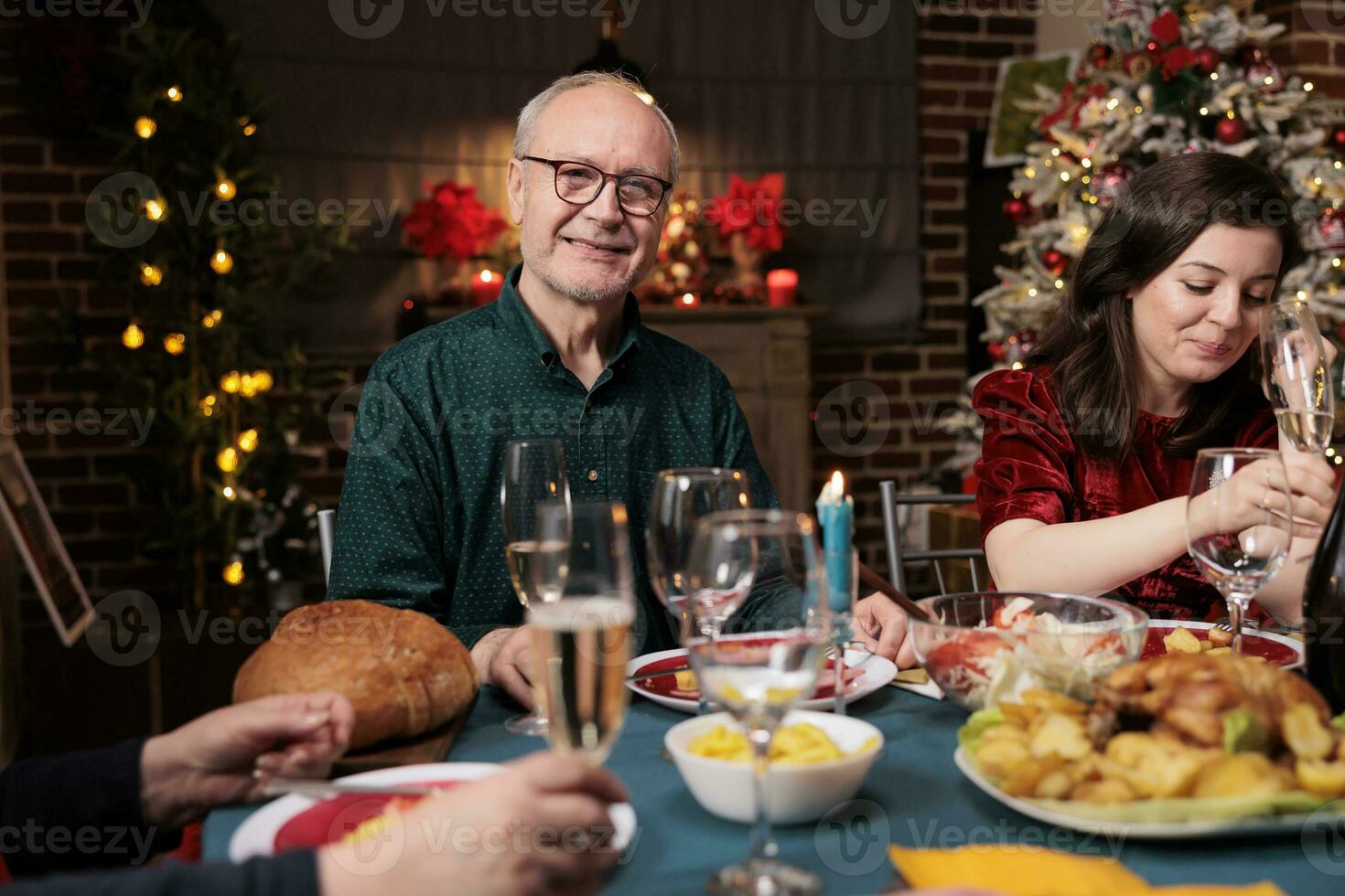 Vovô às jantar mesa com família comendo tradicional refeição e a comemorar Natal feriado às lar. Senior adultos encontro juntos às festivo encontro durante inverno sazonal evento. foto
