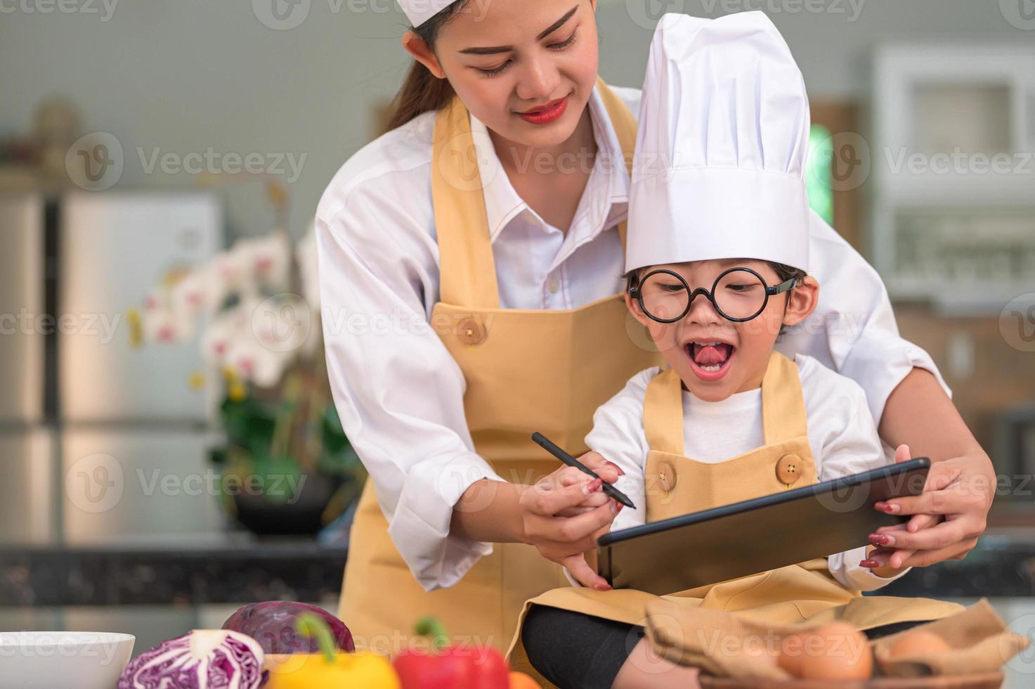 linda mulher asiática e menino bonitinho preparam compras online e listando o ingrediente para cozinhar na cozinha em casa com o tablet. pessoas estilos de vida e família. conceito de comida e ingredientes caseiros foto