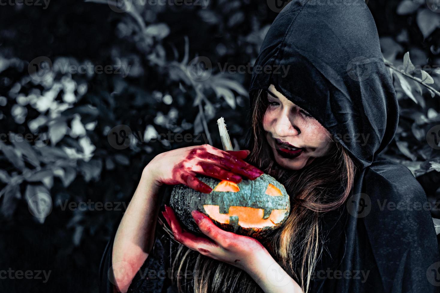 Bruxa demoníaca cuida da abóbora na floresta misteriosa. conceito de fantasma e horror. tema do dia de halloween. sangue vermelho nas mãos de bruxa foto