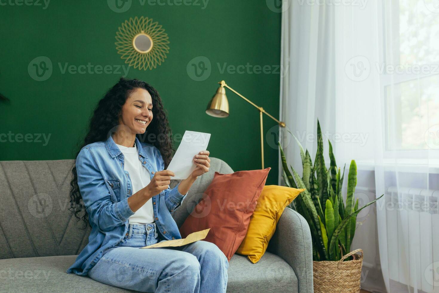 feliz jovem ruivo hispânico mulher recebido uma carta. sentado às casa em a sofá. segurando uma carta com a envelope, leitura, sorridente. foto